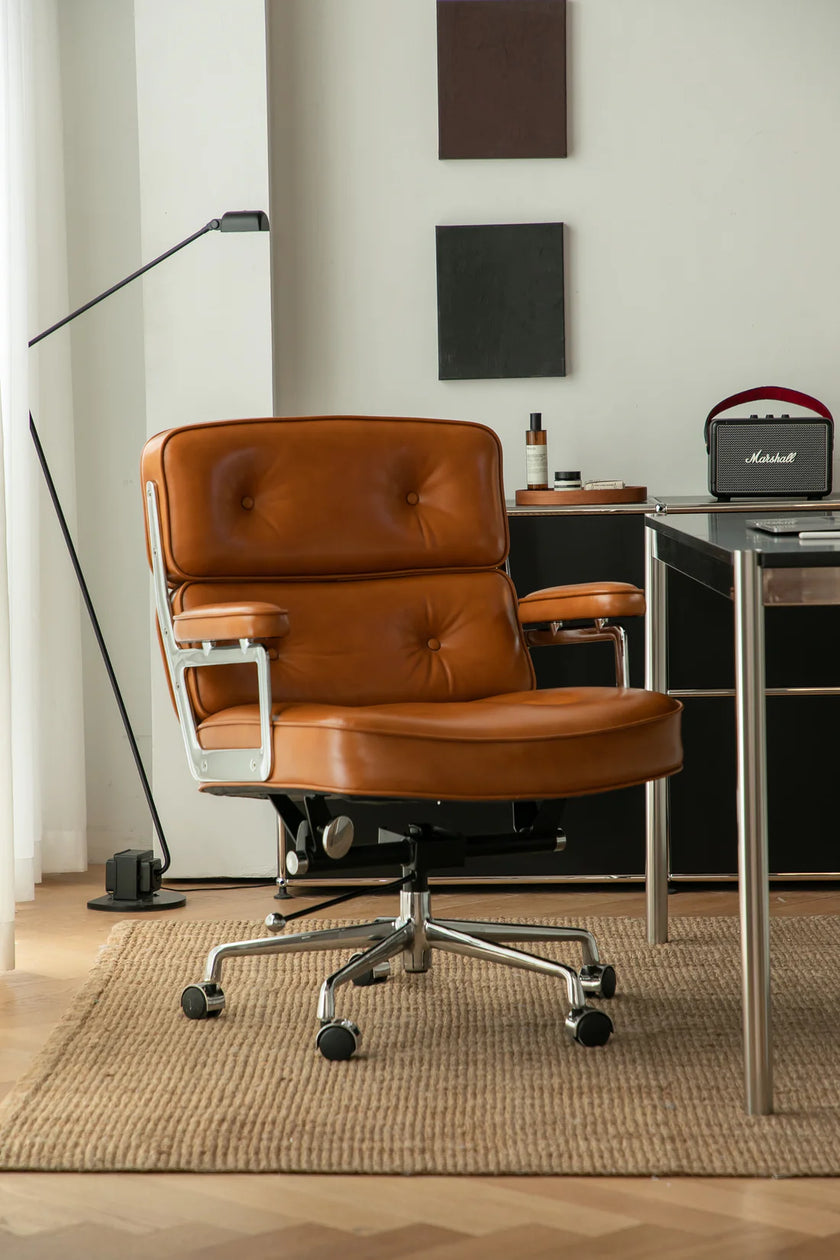 Brown leather office arm chair in a modern office setting with a desk and lamp.