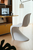 A modern white molded plastic chair in a bright, minimalist home office setting next to a wooden desk with a laptop and a floor lamp.