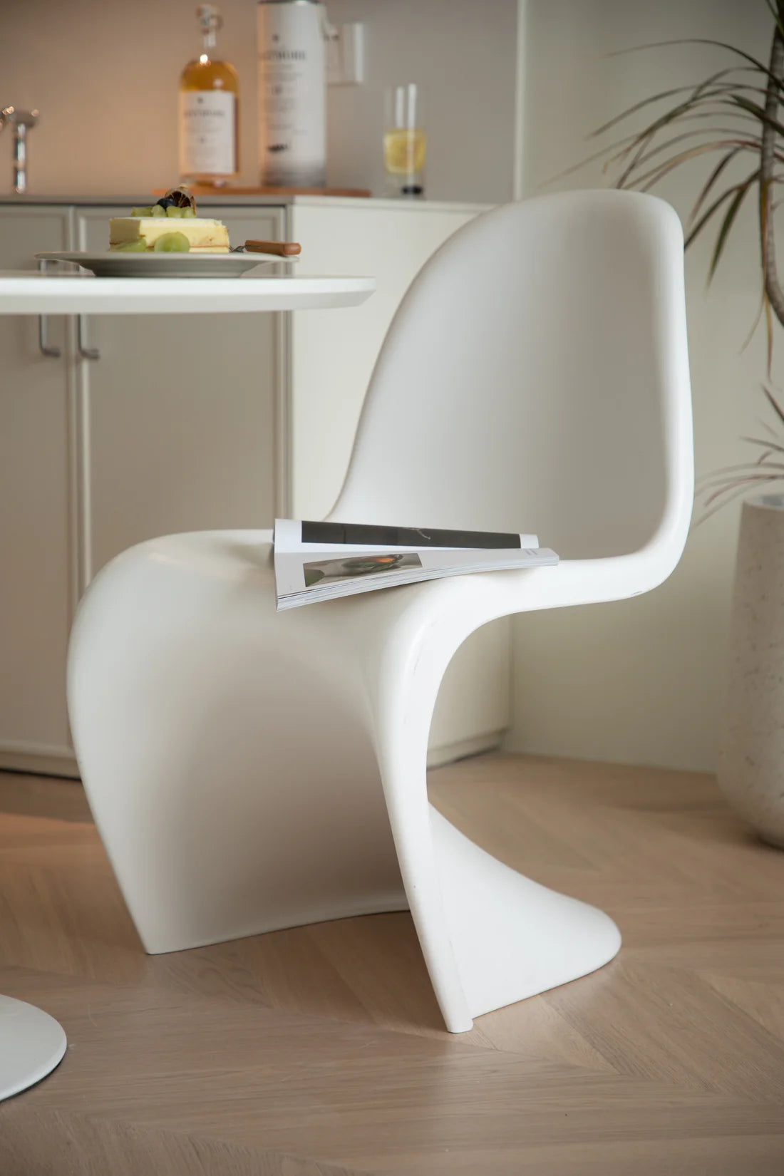 Modern white plastic dining room chair with a magazine on a wooden floor in a minimalistic room.