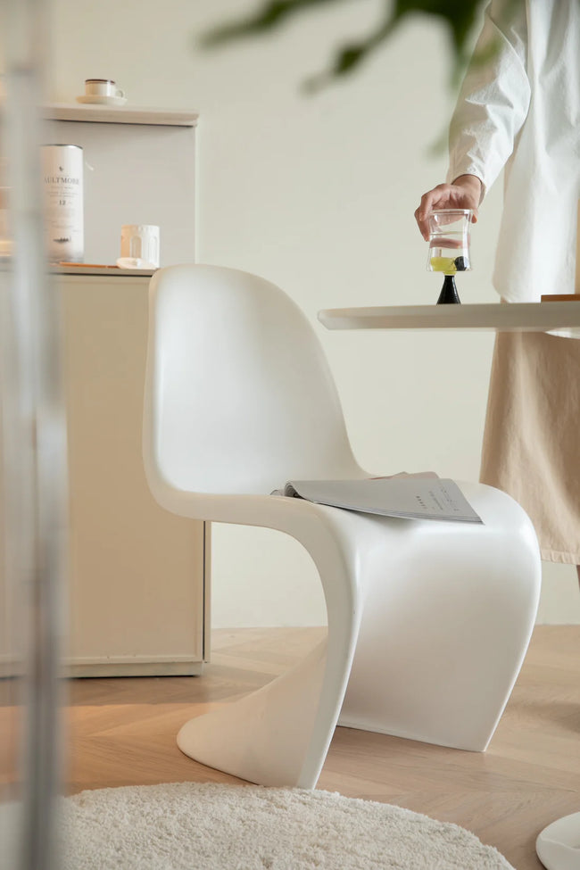 Modern white plastic chair with a person holding a glass of water in a minimalistic room.