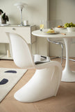 Modern dining room with white plastic dining room chairs and table, and a small table with decorative items in the background.