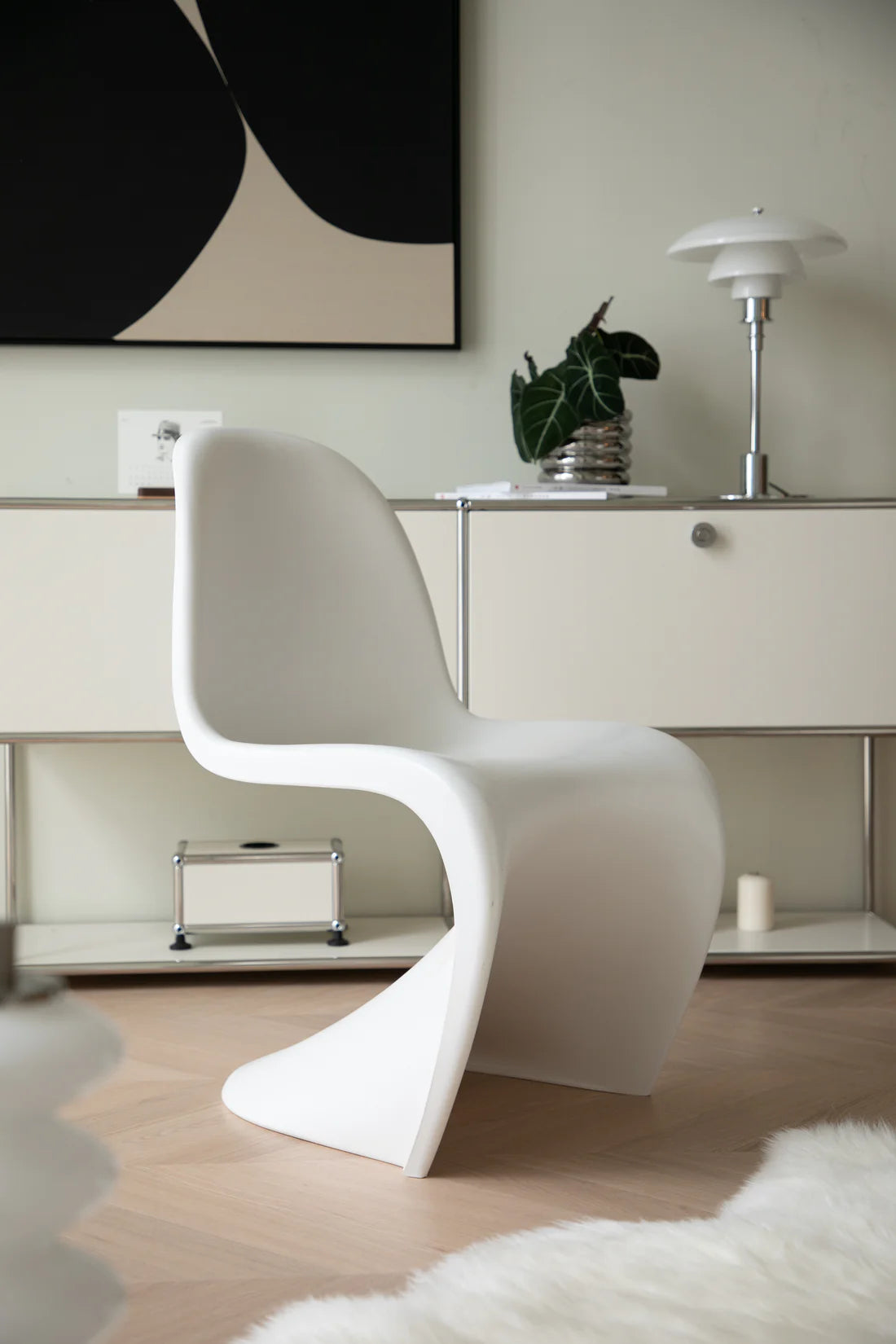 Modern white living room chair in a stylish room with a painting and lamp.