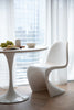 Modern white dining table and plastic dining room chairs in a bright room with large windows.