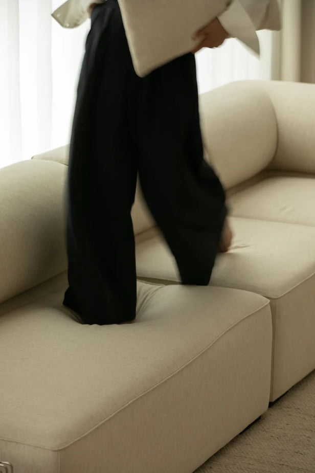 Person wearing black pants and a beige coat standing on a beige sofa.