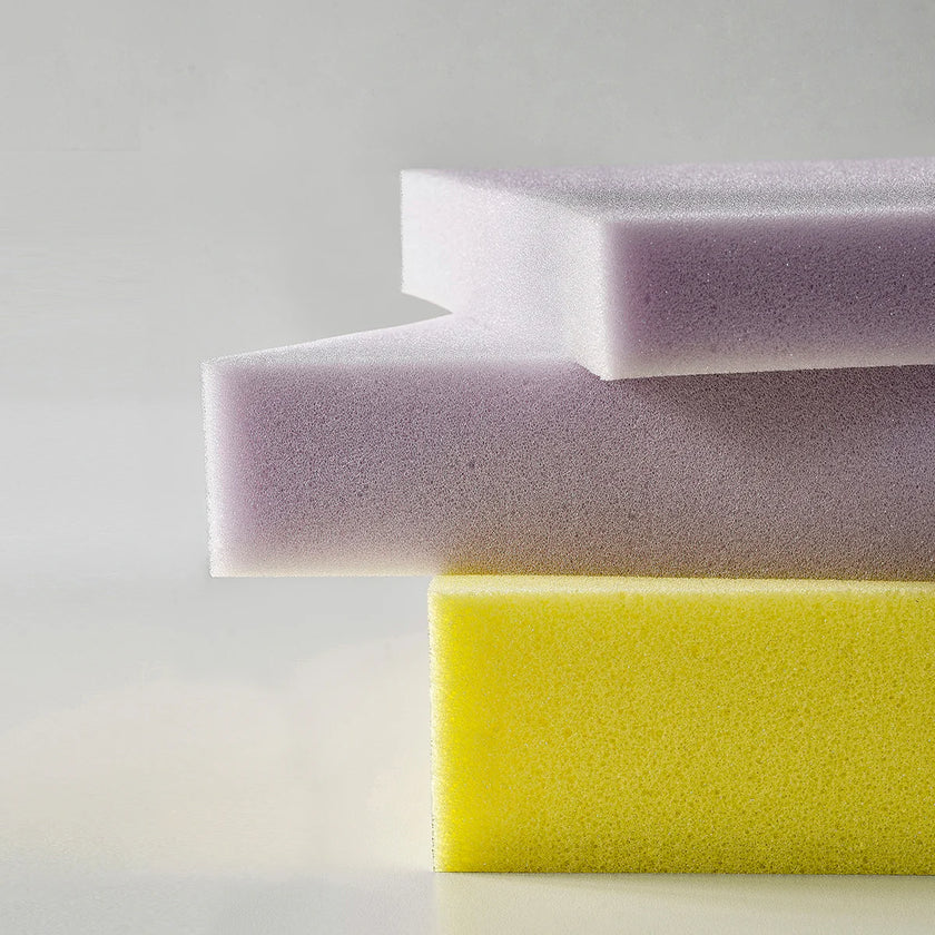 Three sponges of different colors stacked on a light gray background