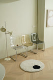 Modern interior with transparent plastic chairs, a floor lamp, and a round rug on wooden flooring.