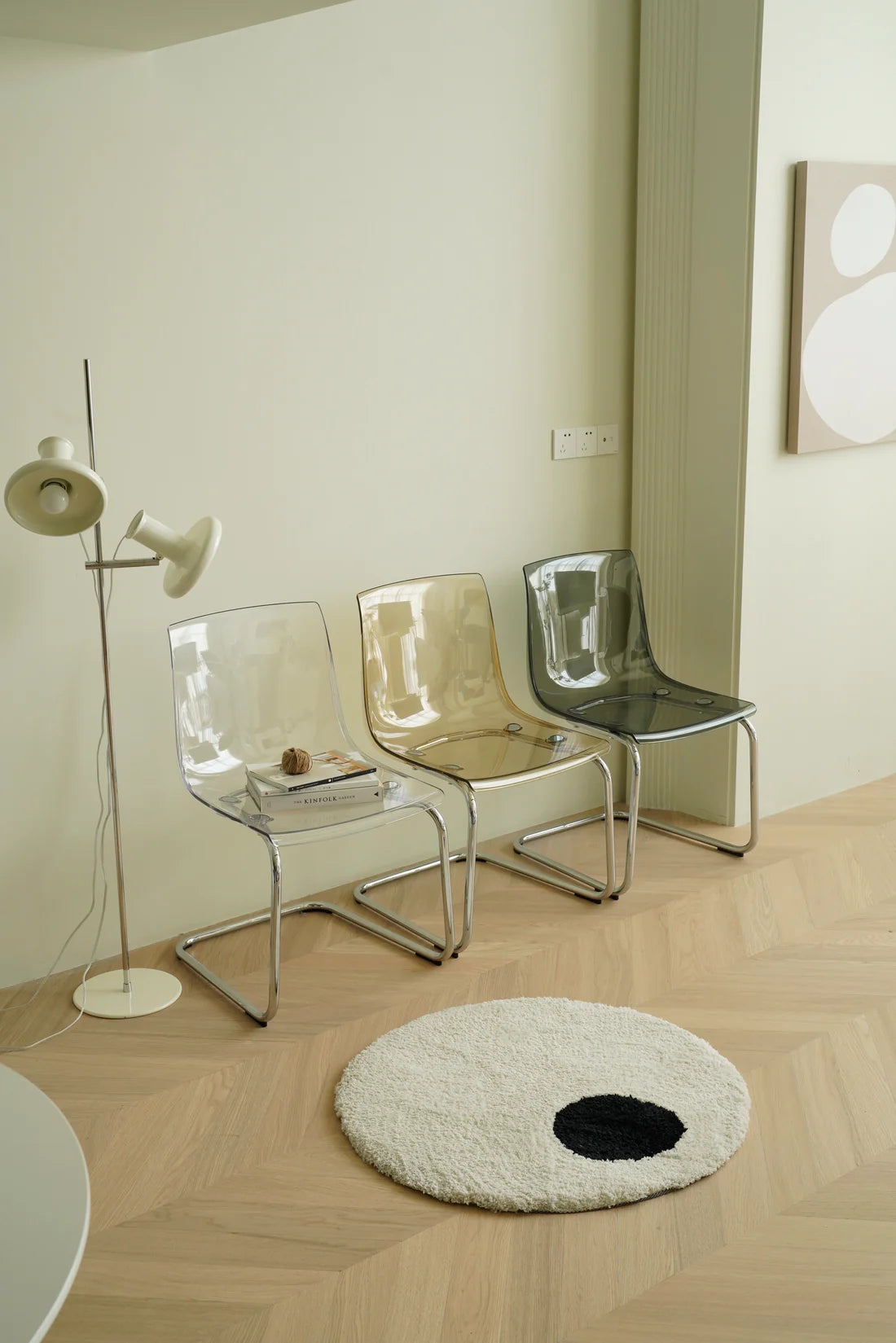 Modern interior with transparent plastic chairs, a floor lamp, and a round rug on wooden flooring.