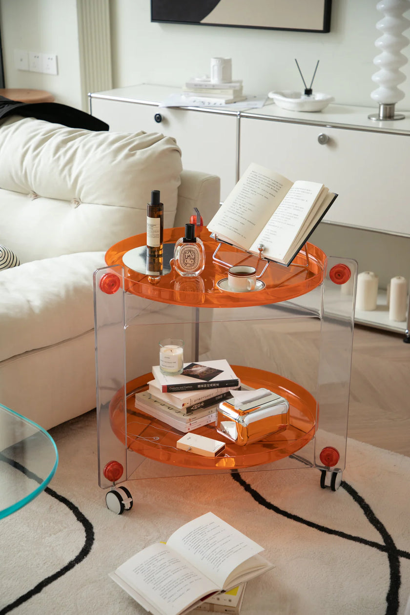 Modern living room with a transparent round side table on wheels, books, and bottles.
