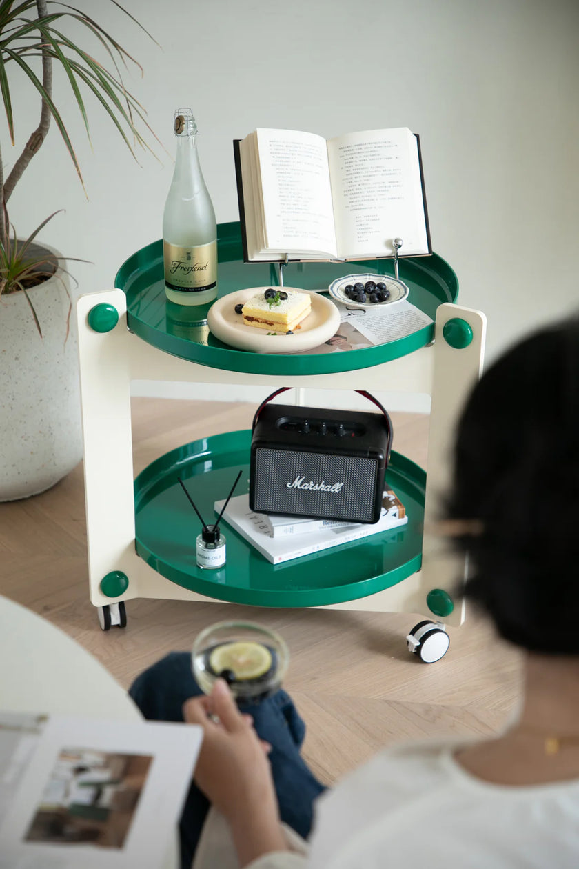 Green and white small side table with a Marshall speaker, bottle, and books in a room.