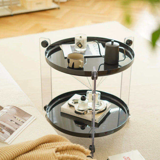 Round black side table with two tiers on a light-colored floor, surrounded by books and a blanket.
