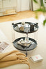Round black side table with two tiers on a light-colored floor, surrounded by books and a blanket.