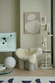 Modern interior with a chair cushions made in wool fabric, round table, and wall art in a neutral color scheme.