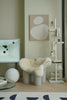 Modern interior with a chair cushions made in wool fabric, round table, and wall art in a neutral color scheme.