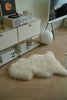 White sheepskin chair cushions on a wooden floor with a record player and decor items in the background.