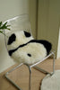 Clear chair with a panda-shaped wool fabric cushion on a light wooden floor.