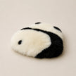 A plush faux-fur accessory with a black and white panda-inspired pattern, photographed on a plain warm beige background.