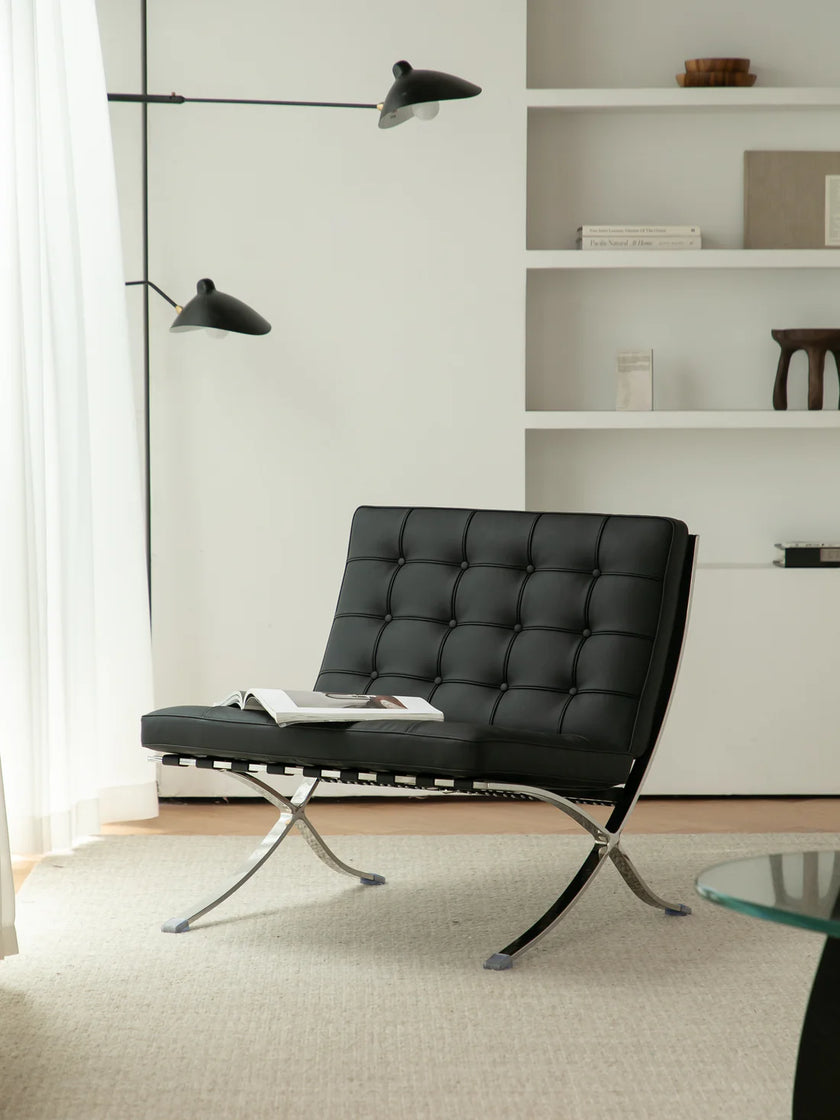 Modern black leather reading chair in a minimalistic living room with white walls and shelves.
