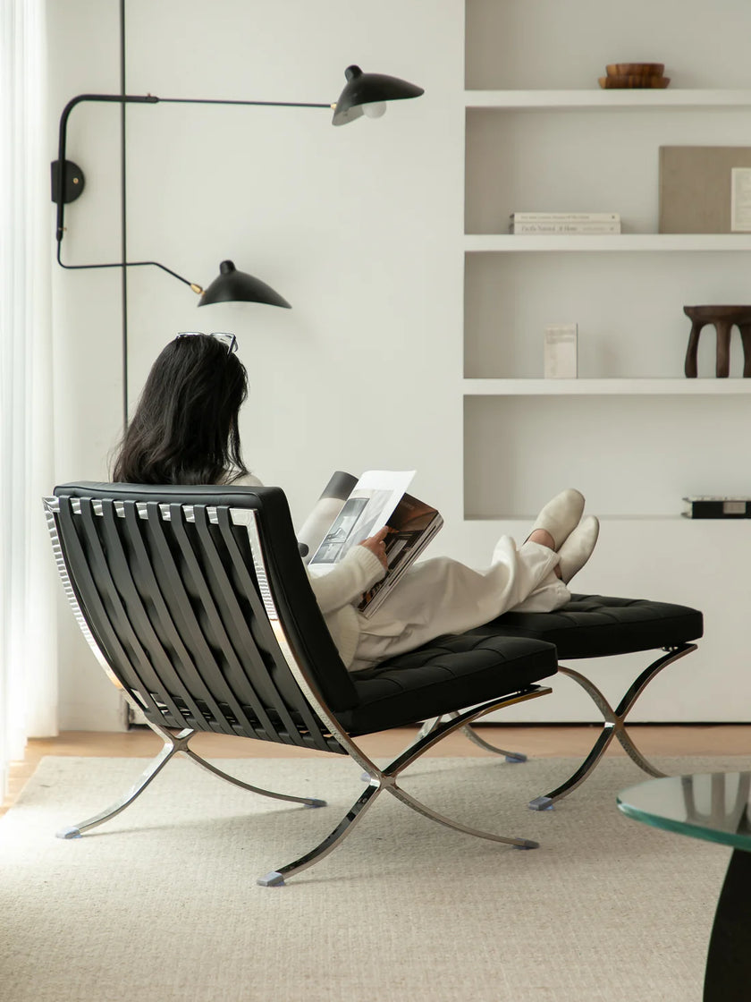 Women reading a book in a modern black metal chair in a minimalistic room.