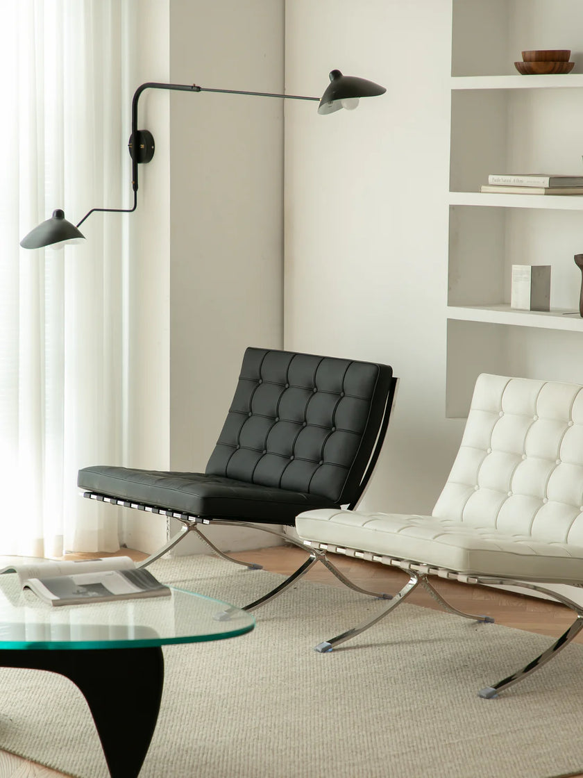 Modern living room with black and white reading chairs, glass table, and wall lights.