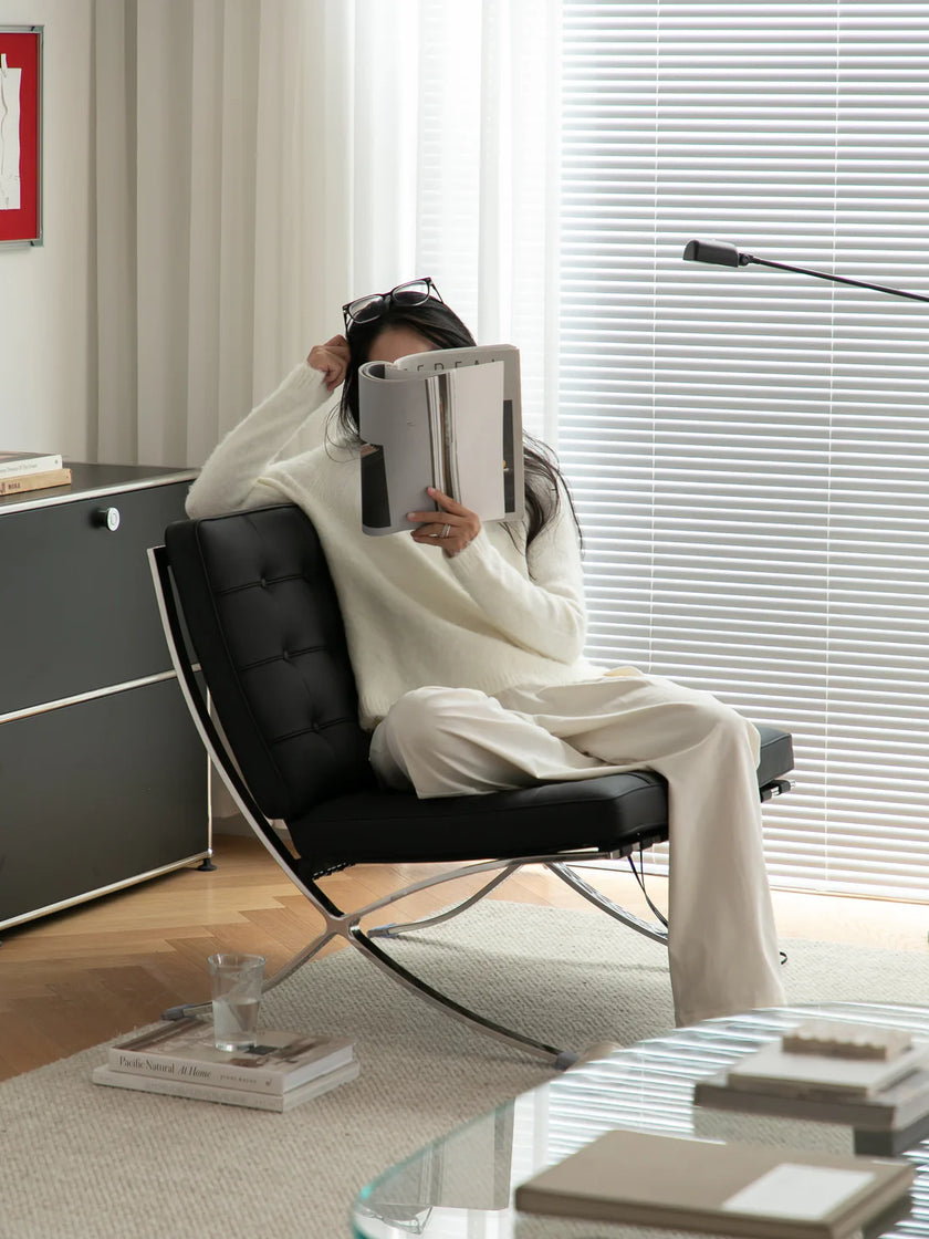 Women sitting in a lounge chair reading a book in a stylish room.