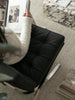 Person sitting on a black leather recliner chair in a room with a rug and books.
