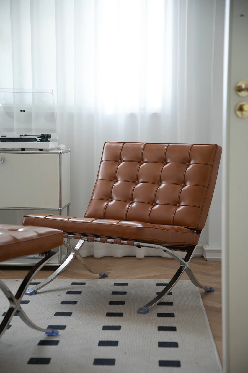 Brown leather bedroom chair on a patterned rug in a room with white curtains.