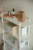White storage shelving unit with a record player, books, and a brown paper bag on a white wall background.