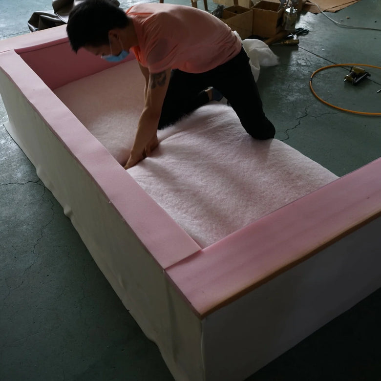 Person assembling a pink and white foam bed frame on a concrete floor.