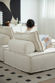 Lady sitting on a beige lounge sofa reading a newspaper in a modern living room.