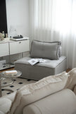 Modern living room with gray small sectional sofa, white curtains, and a glass coffee table.