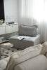 Modern living room with gray small sectional sofa, white curtains, and a glass coffee table.