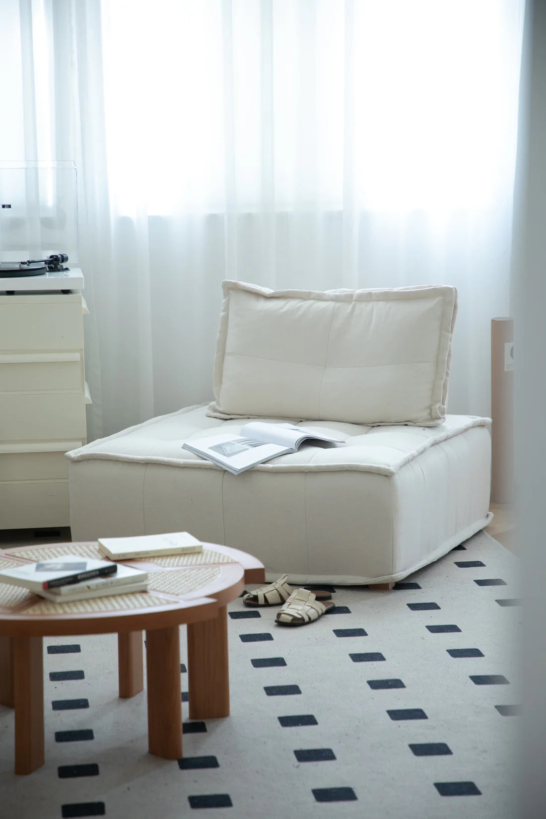 White lounge sofa with a pillow and a small table in a room with white curtains.