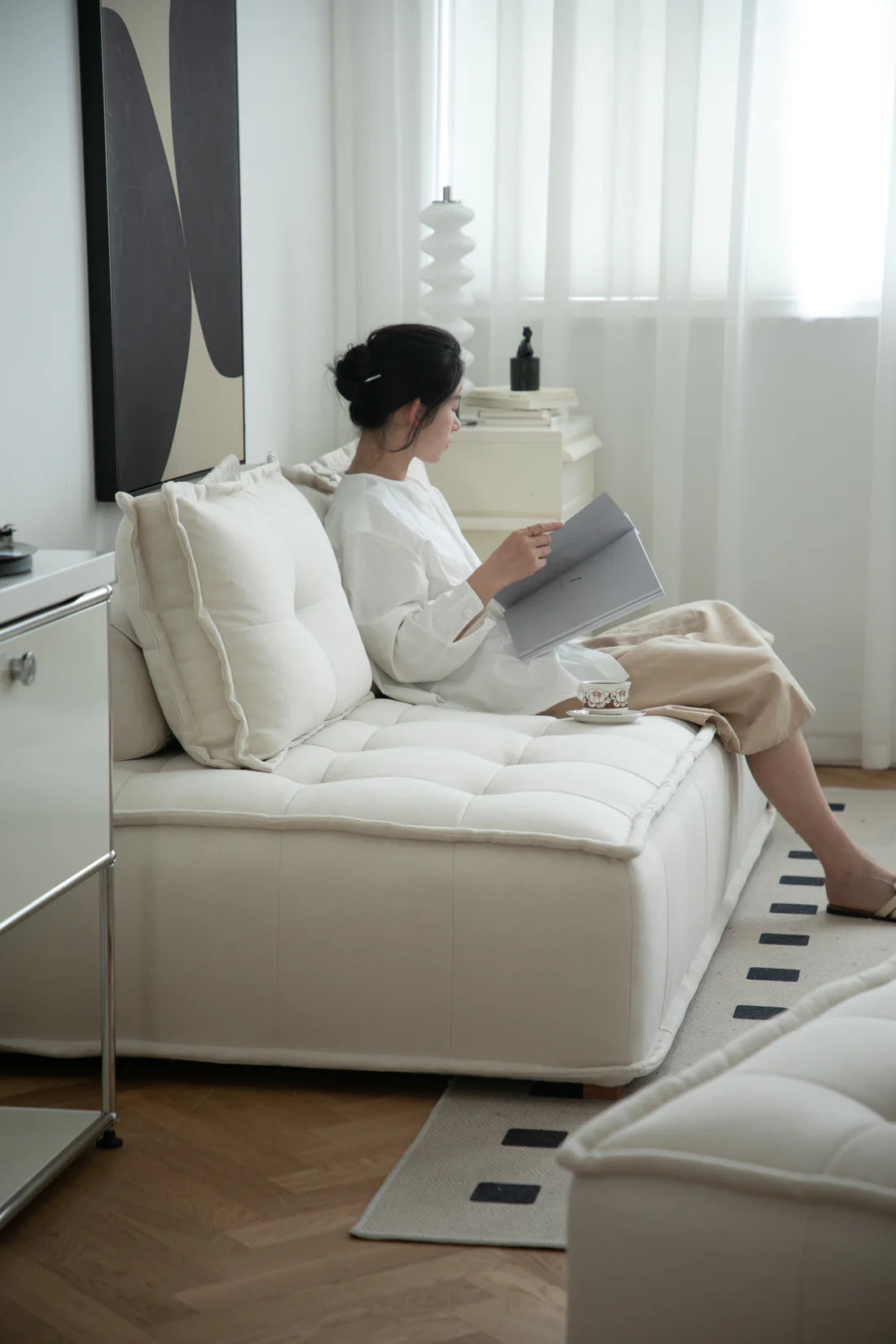Lady sitting on a white sofa reading a book in a modern living room.