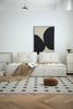 Modern living room with a white love seat sofa, abstract art, and geometric rug.