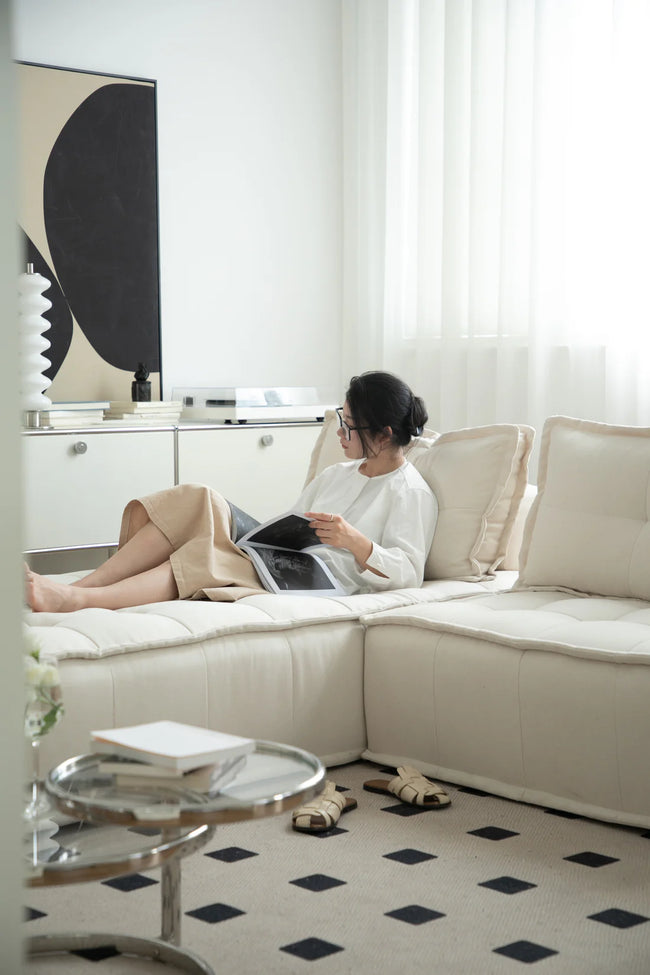 Lady reading a book on a beige sectional sofa in a modern living room.