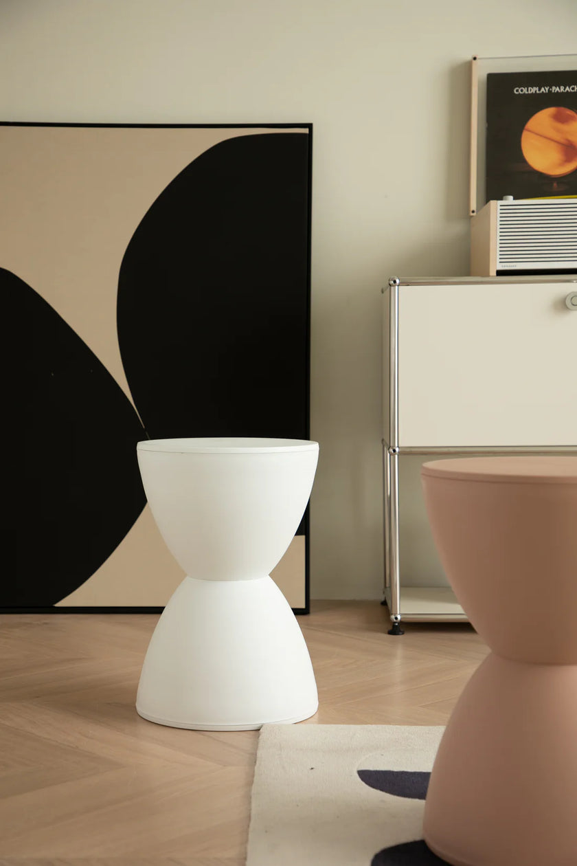 Modern interior with white and pink shower stools, a black and white abstract painting, and a white cabinet.