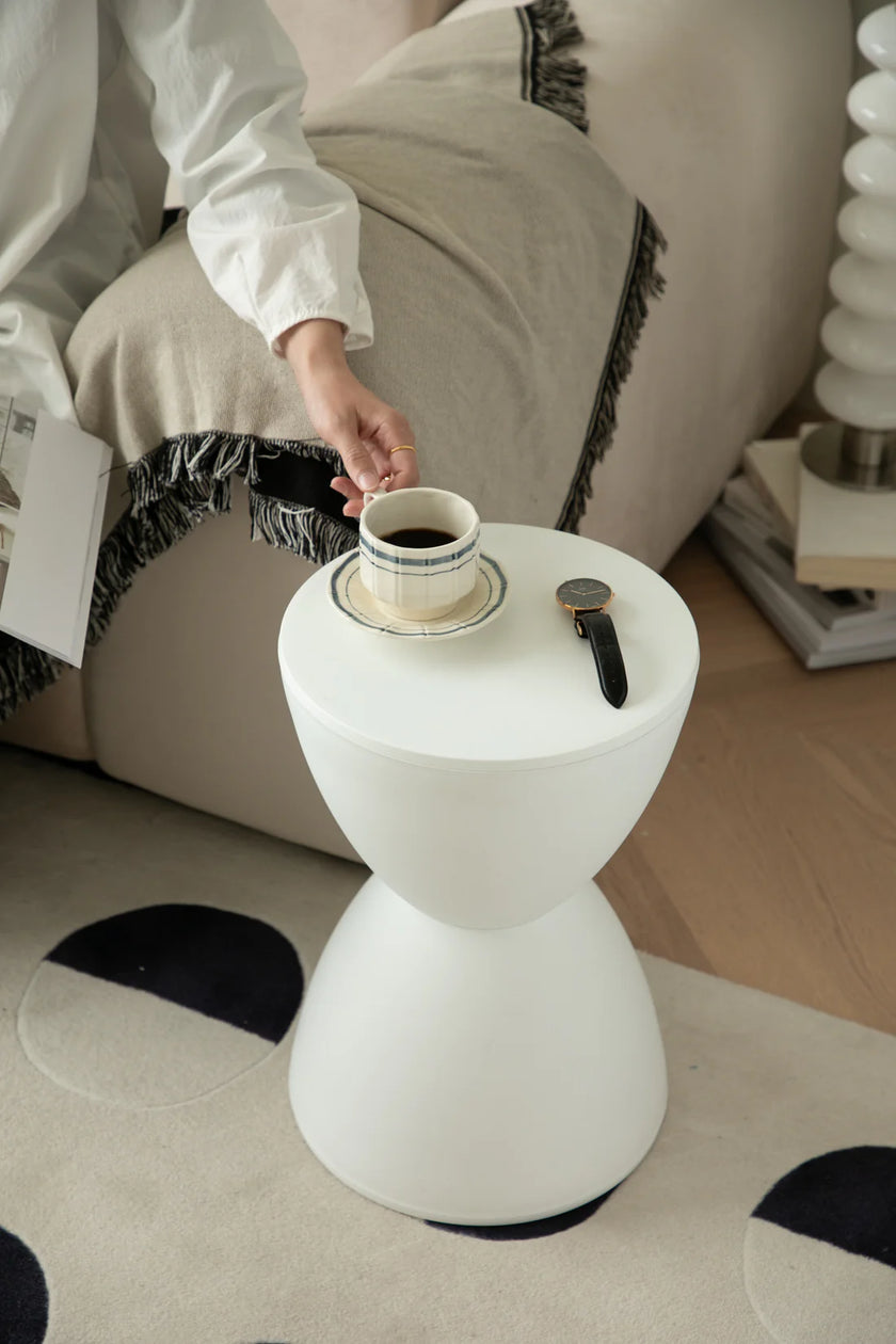 Lady placing a cup of coffee on a small white stool in a cozy living room.