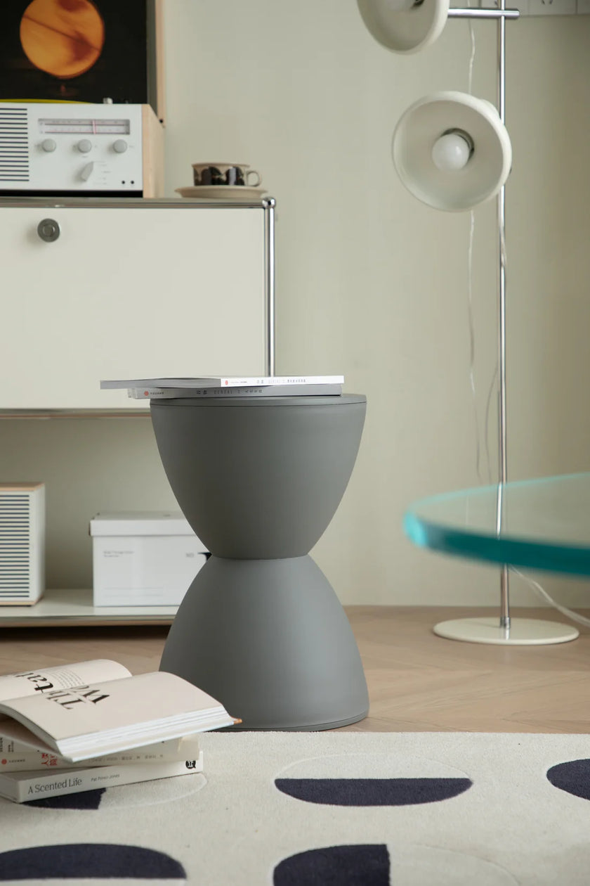 Gray bathroom stool in a room with a rug, books, and a lamp.
