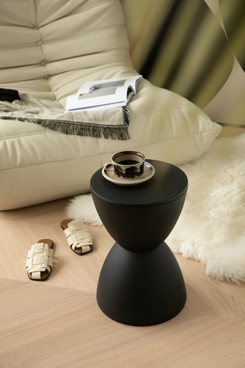 Black stool side table with a cup and saucer next to a beige sofa.