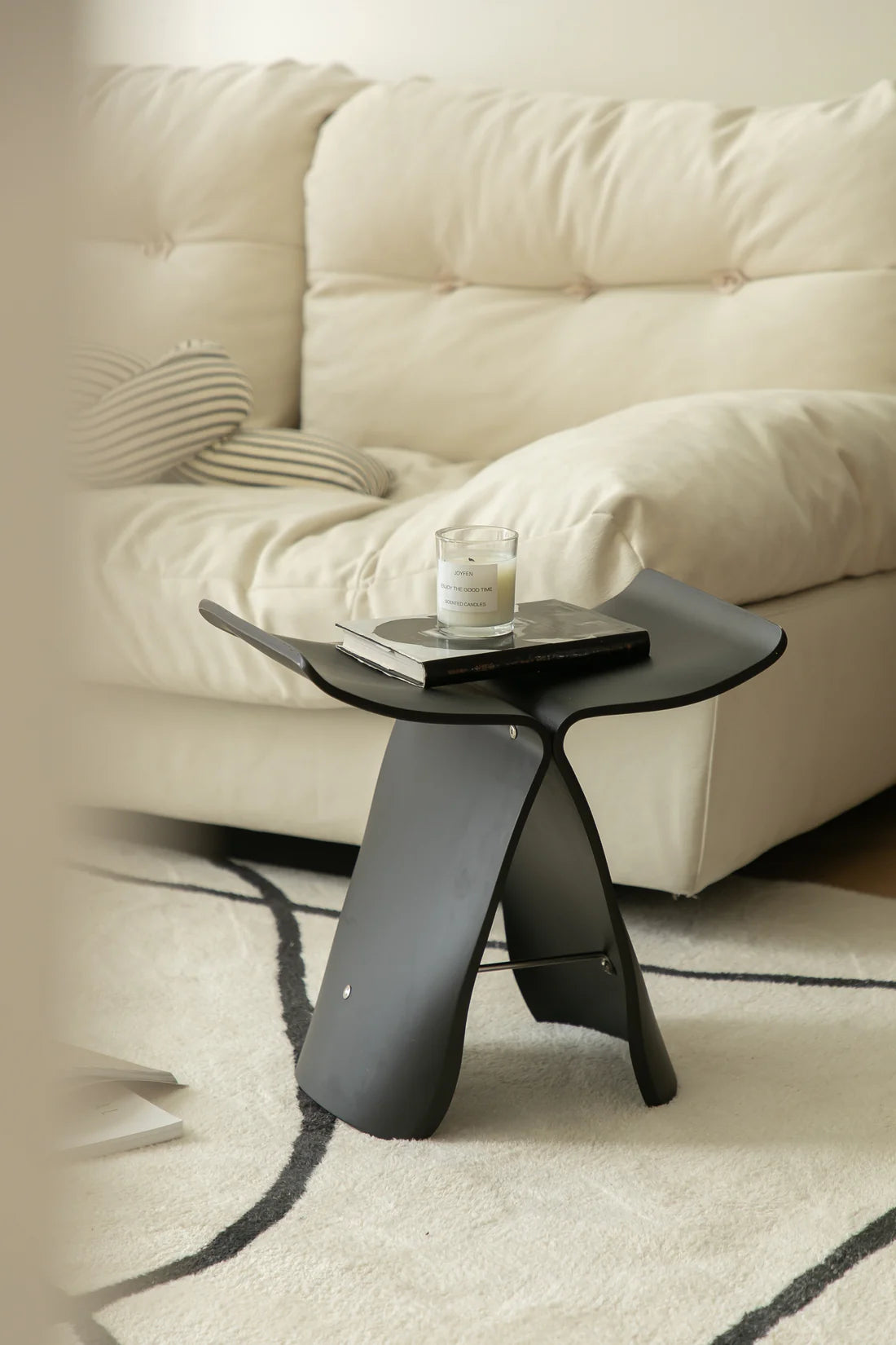 Modern black wooden stool with a glass of water and book in front of a beige sofa.
