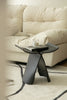 Modern black wooden stool with a glass of water and book in front of a beige sofa.