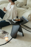 Lady sitting on a couch with a small black stool holding a teapot and a candle.