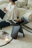 Lady sitting on a couch with a small black stool holding a teapot and a candle.
