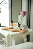 Square coffee table with a wooden cutting board, glass vase with pink flowers, and books in a room.