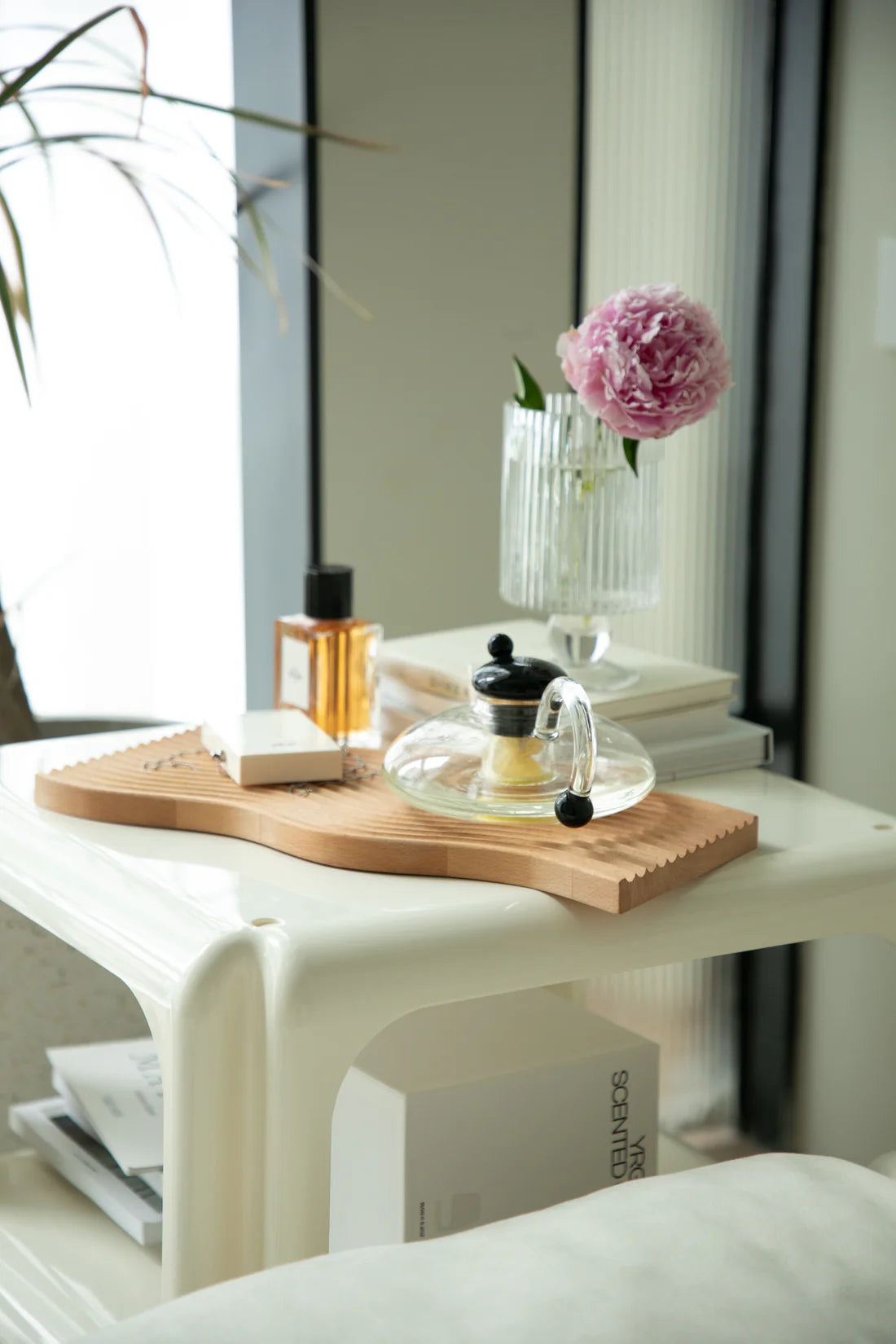 Square coffee table with a wooden cutting board, glass vase with pink flowers, and books in a room.