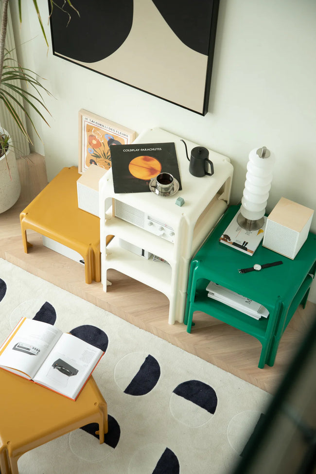 Small living room with a white modular coffee table, green table, and yellow square coffee table on a patterned rug.