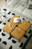 Yellow modular square coffee table with books and decorative items on a patterned rug.