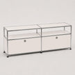 A modern modular storage cabinet with a chrome metal frame, clear glass shelves, and white drawer fronts with round silver knobs, set against a plain light gray background.