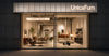 UnicaFurn furniture showroom storefront at night, with large glass windows displaying an elegantly furnished interior in warm lighting. The brand name 'UnicaFurn' is prominently lit above the entrance.
