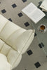 White lounge chair with a glass coffee table featuring an open book and a cup of coffee on a patterned rug.